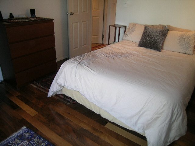 Furnished 1-bedroom + den with hardwood floors and a cozy bed setup. - 1403 - 907 Beach Avenue, Vancouver Downtown
