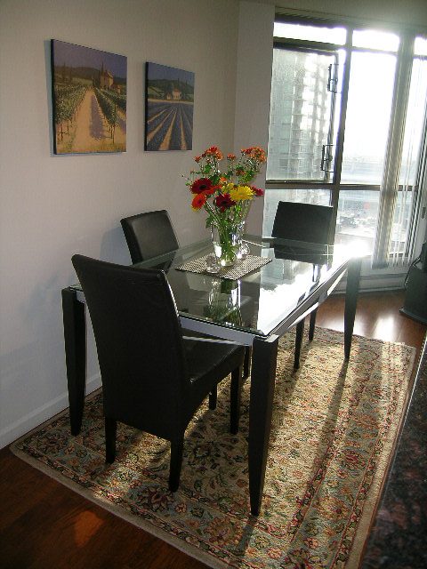 Furnished dining area with a glass table, black chairs, and a floral centerpiece on a patterned rug. - 1701 - 867 Hamilton Street, Vancouver Downtown