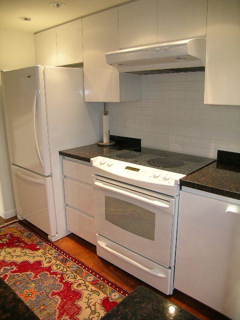 Bright kitchen with white appliances, granite countertops, hardwood floors, and a red patterned rug. - 1701 - 867 Hamilton Street, Vancouver Downtown