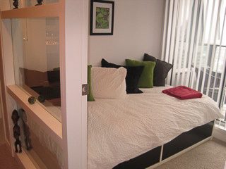 Bright and cozy 1-bedroom + den with a modern design, featuring a comfortable bed with green pillows and a large window...
