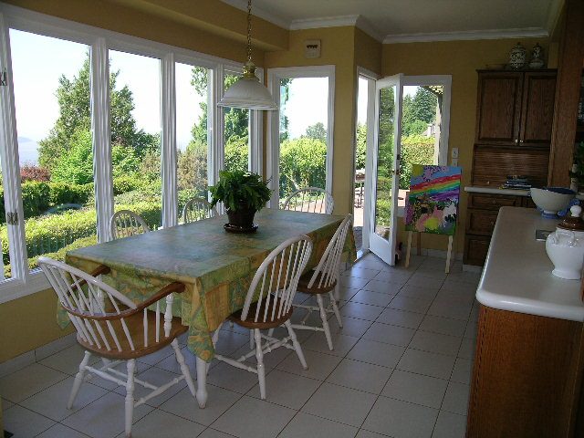 Bright dining area with large windows, greenery outside, and wooden chairs. - 1332 Camridge Place, West Vancouver