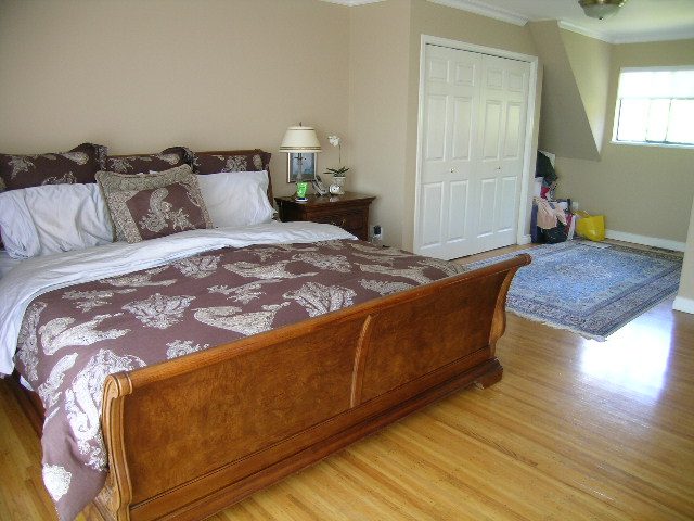 Bright bedroom with wooden sleigh bed, hardwood floors, and a white closet door. - 1332 Camridge Place, West Vancouver