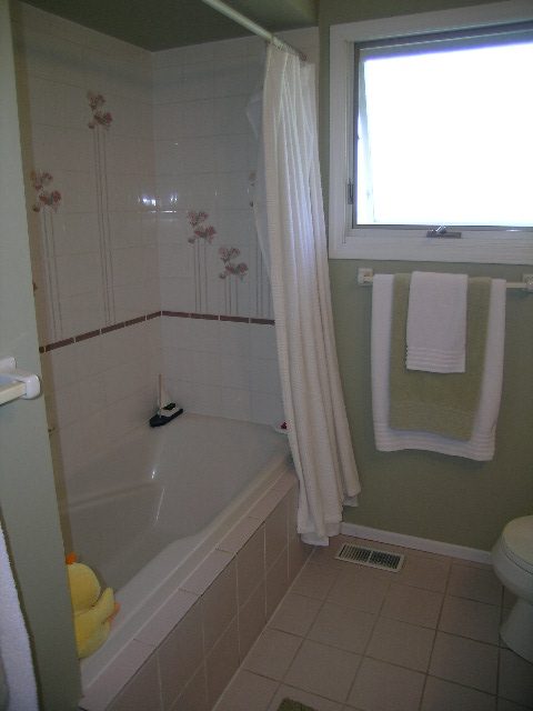 Bright bathroom with tiled walls, shower curtain, and window letting in natural light. - 1332 Camridge Place, West Vancouver