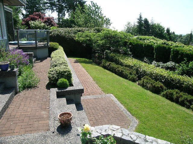 Furnished patio with brick walkway, lush greenery, and a view of trees. - 1332 Camridge Place, West Vancouver