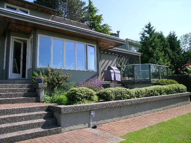 Furnished living room with large windows, brick patio, and lush garden. - 1332 Camridge Place, West Vancouver