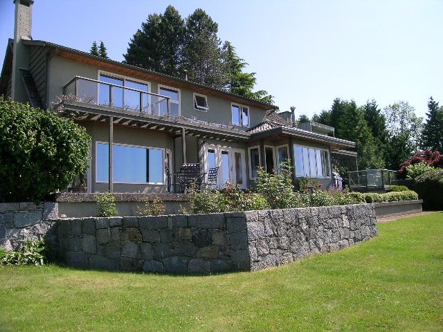 Furnished 3-bedroom house with stone walls and large windows, surrounded by greenery. - 1332 Camridge Place, West Vancouver
