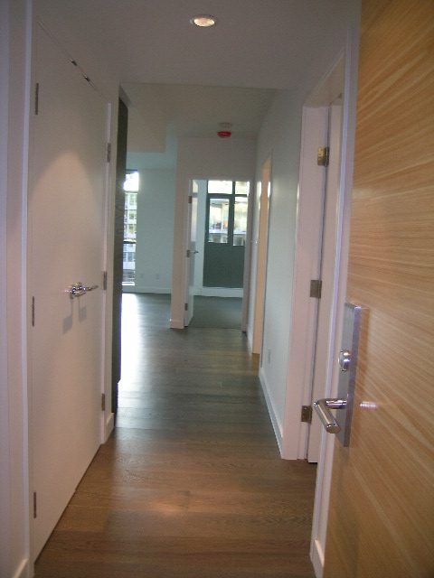 Bright hallway with wooden floors and white walls, leading to a den area with a city view. - 602 - 5782 Berton Avenue, Vancouver West Side