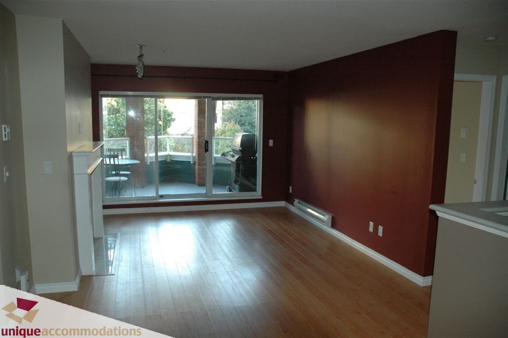 Bright living room with hardwood floors and a large window leading to a patio. - 208 - 128 West 8th Street, North Vancouver