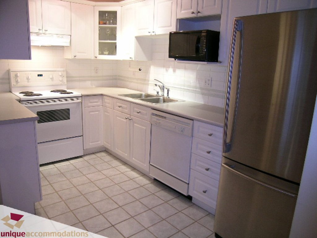 Bright kitchen with white cabinets, stainless steel appliances, and tiled flooring. - 208 - 128 West 8th Street, North Vancouver