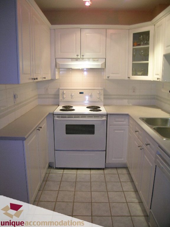 Bright kitchen with white cabinets, tiled backsplash, and a white stove. - 208 - 128 West 8th Street, North Vancouver