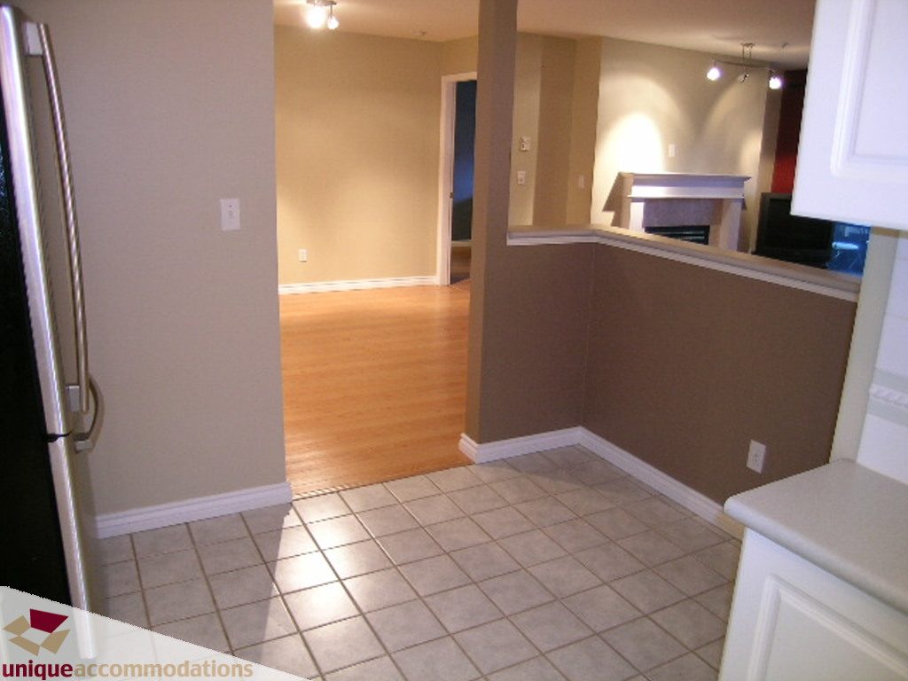 Bright kitchen with tiled floor and white countertops, leading to a living area with hardwood floors. - 208 - 128 West 8th Street, North Vancouver