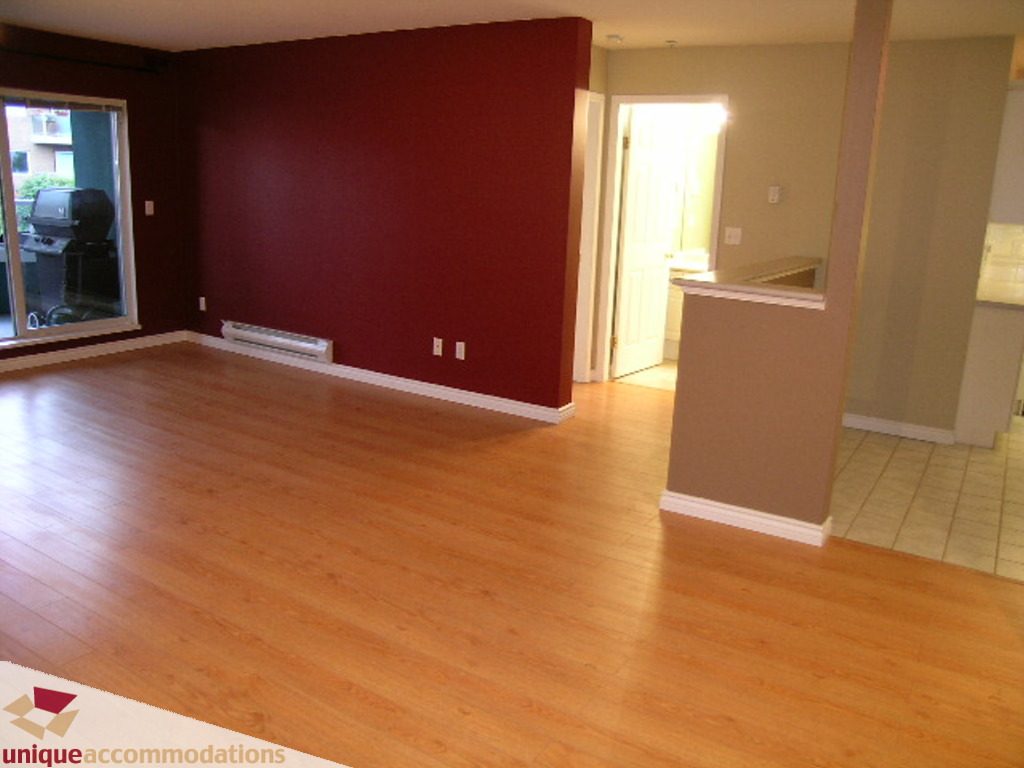 Bright living room with hardwood floors and a red accent wall. - 208 - 128 West 8th Street, North Vancouver