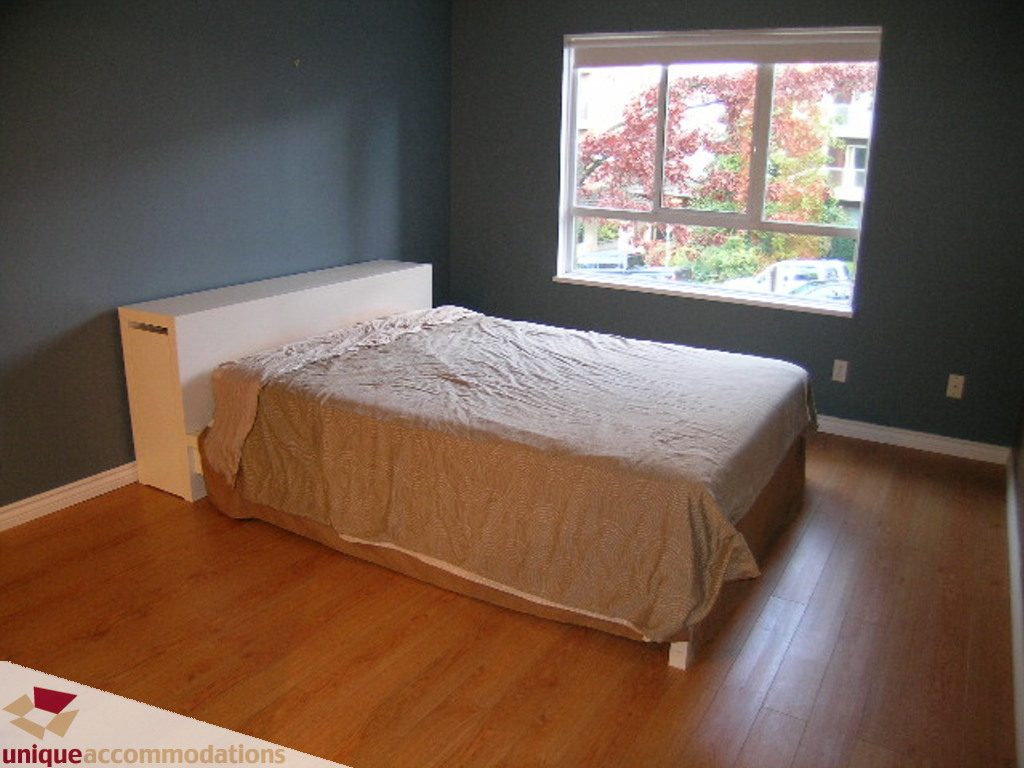 Furnished bedroom with hardwood floors and a city view. - 208 - 128 West 8th Street, North Vancouver