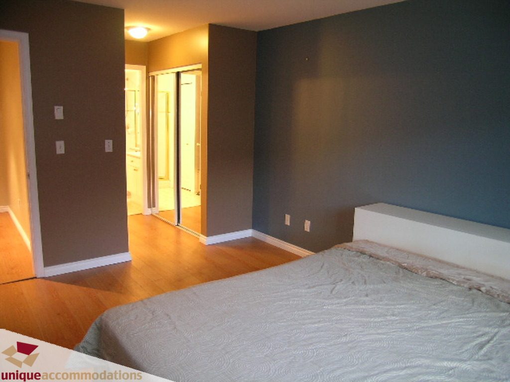 Furnished bedroom with hardwood floors and a large bed. - 208 - 128 West 8th Street, North Vancouver