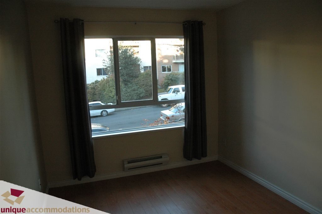 Bright living room with hardwood floors and a city view through large windows. - 208 - 128 West 8th Street, North Vancouver