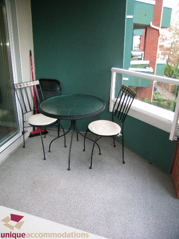 Furnished balcony with metal table and chairs, carpeted floor, brick wall backdrop. - 208 - 128 West 8th Street, North Vancouver