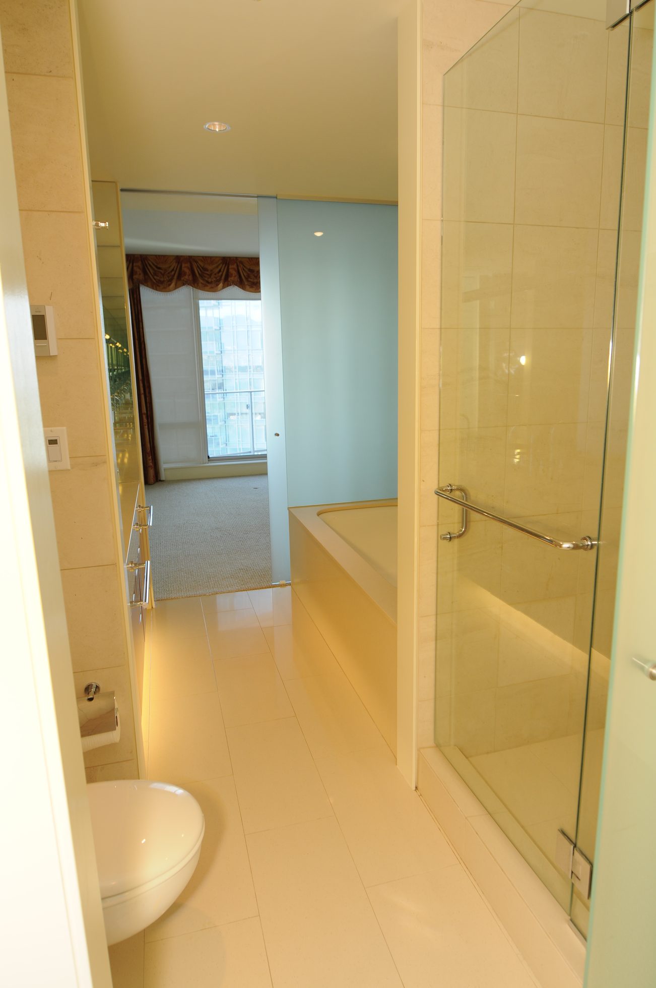 Bright bathroom with modern shower and large bathtub, leading to a cozy bedroom with city view. - 2304 - 1077 West Cordova St, Vancouver Downtown