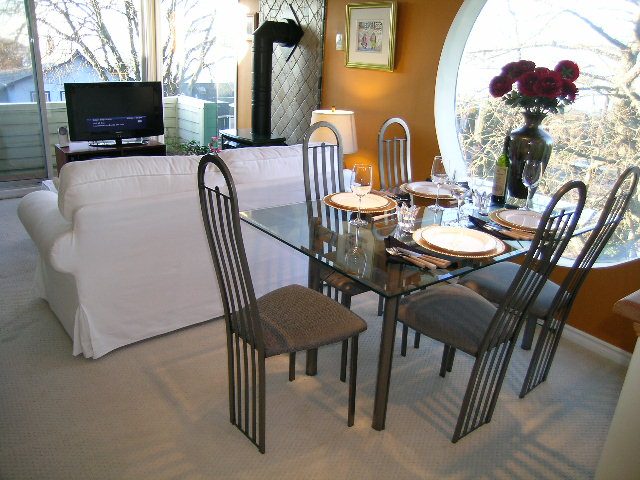 Open dining area with glass table, white slipcovered furniture, and large windows with city view. - 1628 Stephens Street, Vancouver West Side