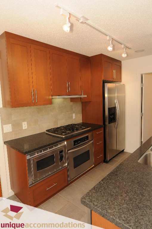 Bright kitchen with granite countertops, stainless steel appliances, and wooden cabinets. - 1802 - 1189 Melville Street, Vancouver Downtown
