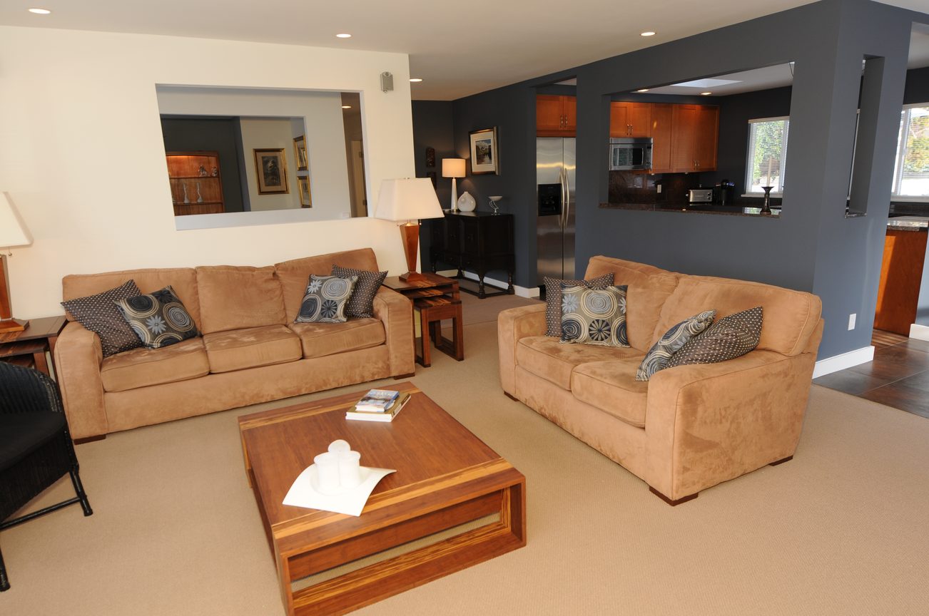 Spacious living room with beige sofas, wooden coffee table, and kitchen counter in background. - 4196 Norwood Avenue, North Vancouver