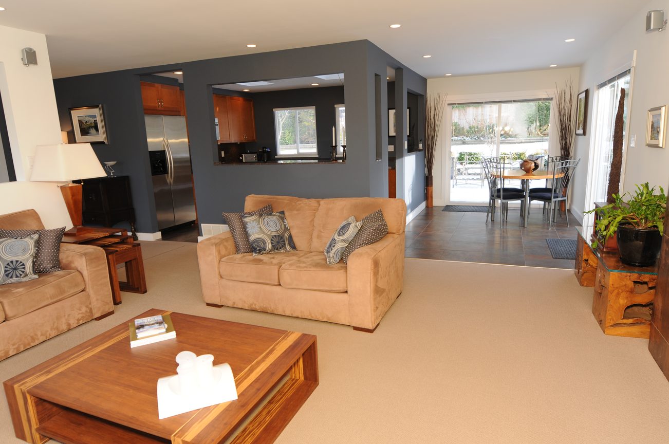 Bright living room with beige couches, hardwood floors, and a view of the kitchen and dining area. - 4196 Norwood Avenue, North Vancouver