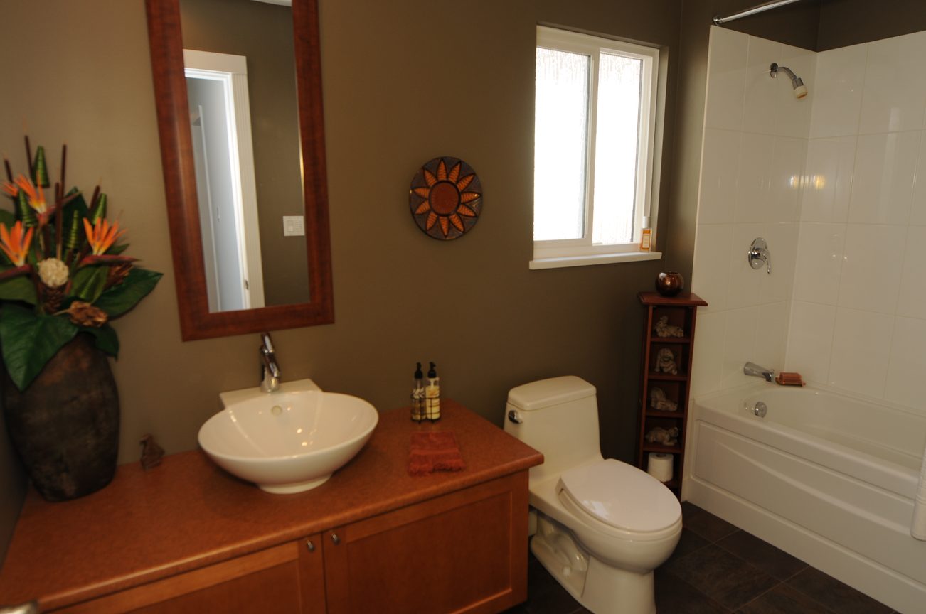 Bright bathroom with wooden vanity, sunburst wall art, and a large window. - 4196 Norwood Avenue, North Vancouver