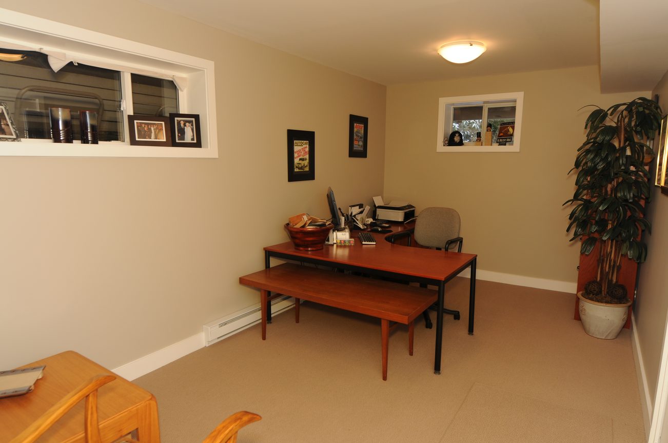 Furnished living room with wooden furniture and a desk area, featuring a large window and a potted plant. - 4196 Norwood Avenue, North Vancouver