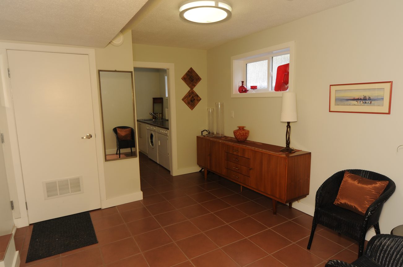 Bright living room with wood-paneled sideboard and red vase, leading to a kitchen with stainless steel appliances.