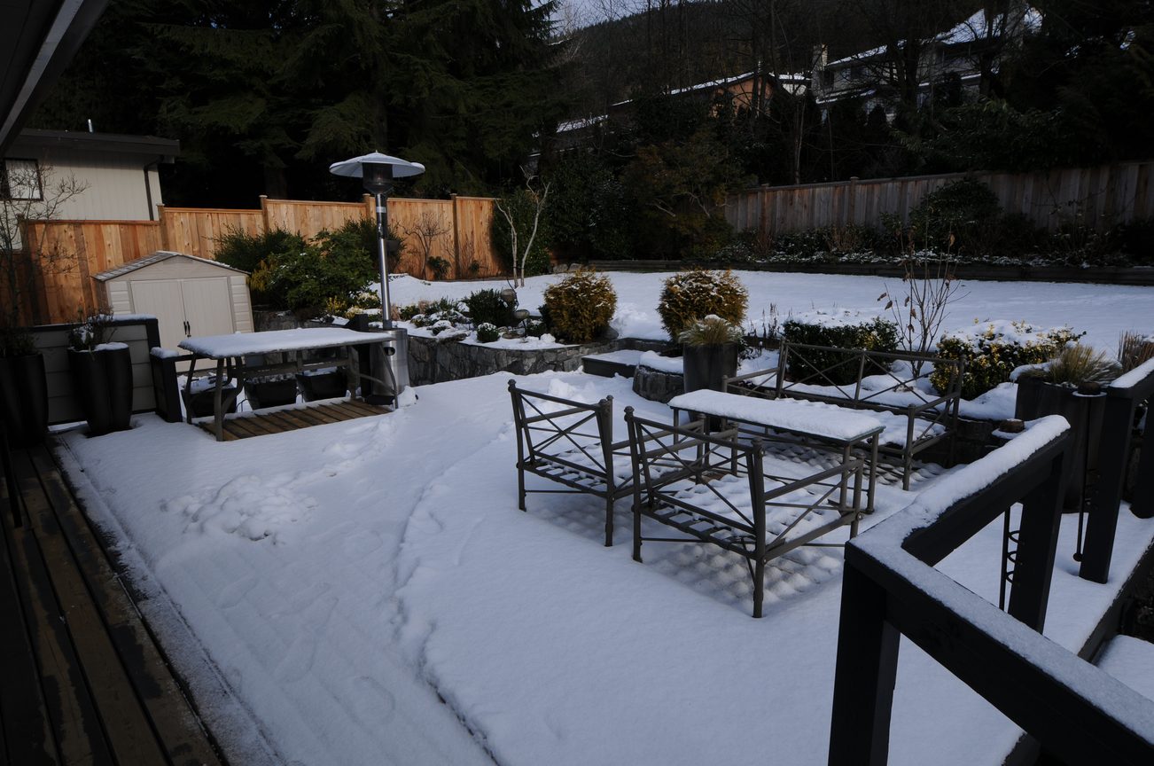 Furnished patio with snow-covered furniture and wooden deck, surrounded by trees and a wooden fence. - 4196 Norwood Avenue, North Vancouver
