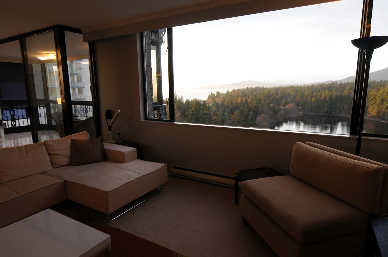 Bright living room with large windows offering a scenic view of the forest and water, furnished with a sectional sofa and...