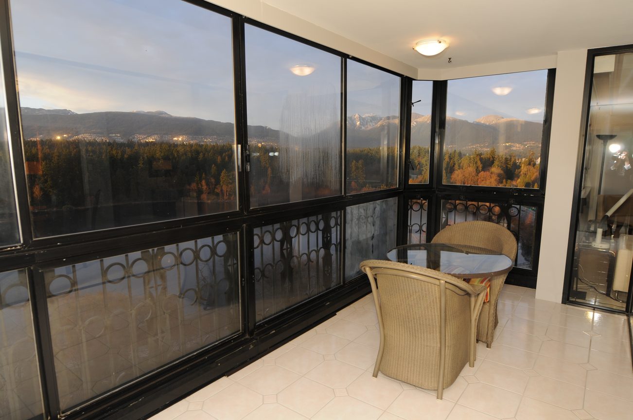 Bright dining area with large windows showcasing a stunning city view and mountains, featuring a glass table and wicker...