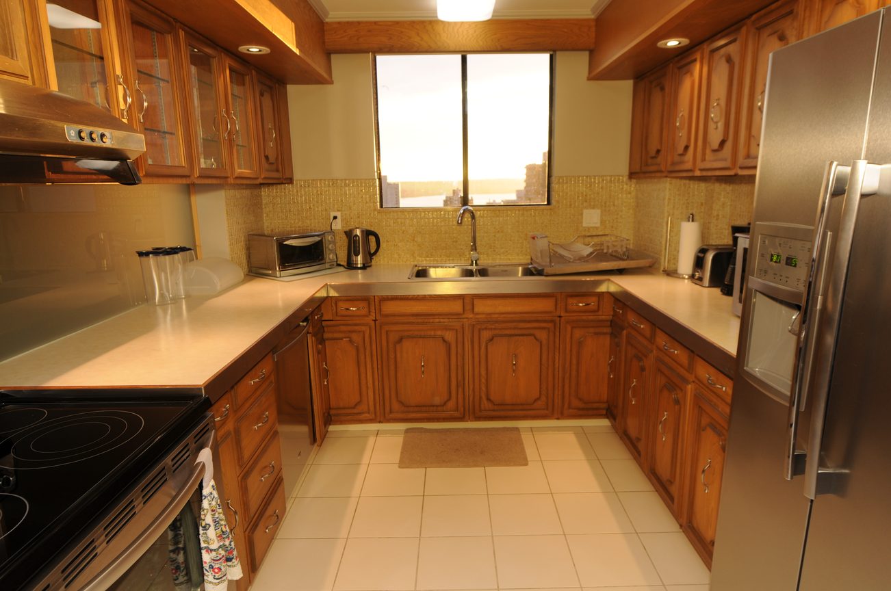 Bright kitchen with wooden cabinets, stainless steel appliances, and a city view through the window. - 1501 - 845 Chilco Street, Vancouver Downtown