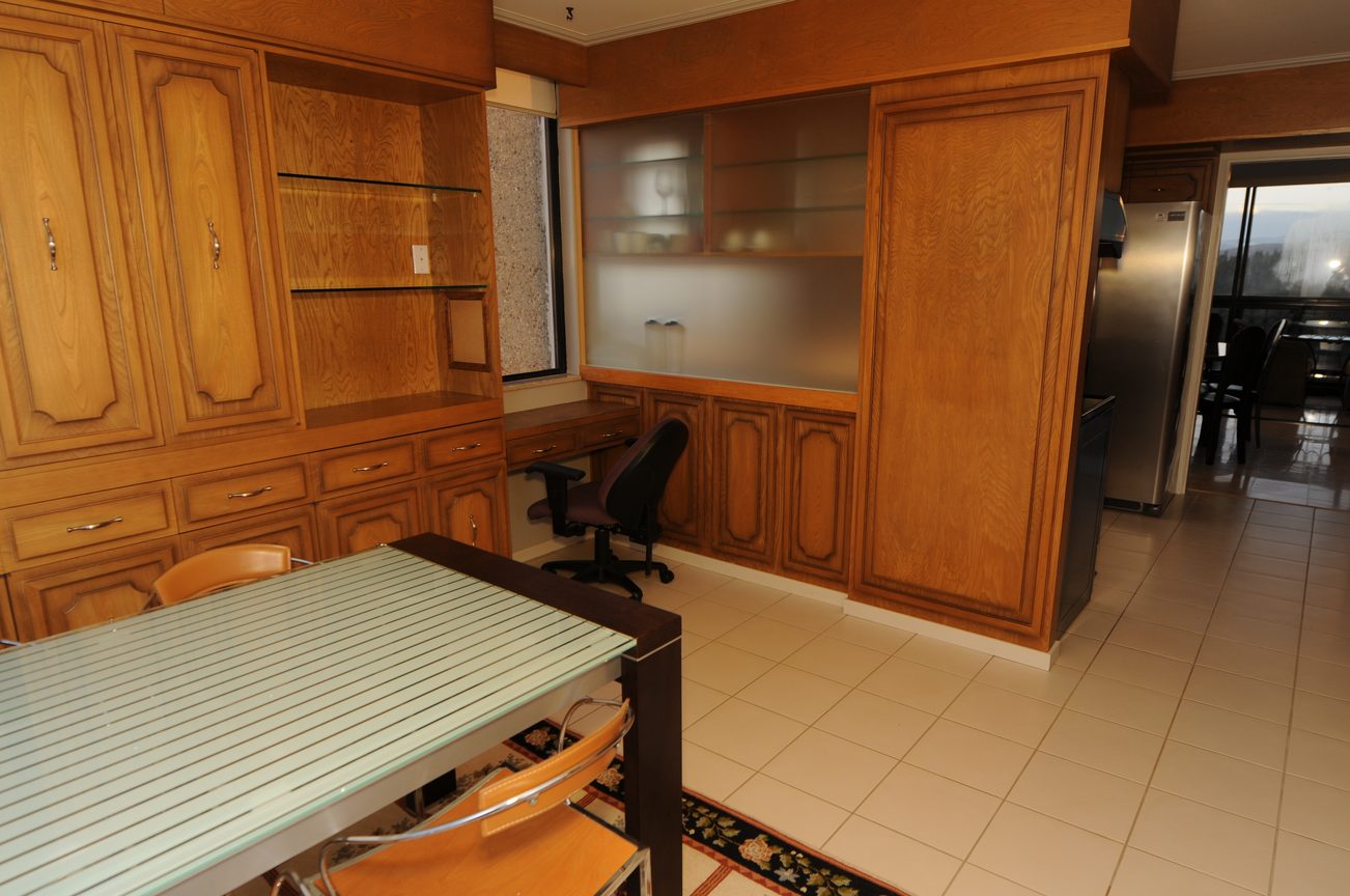 Furnished kitchen with wooden cabinetry and glass countertops, city view through window. - 1501 - 845 Chilco Street, Vancouver Downtown