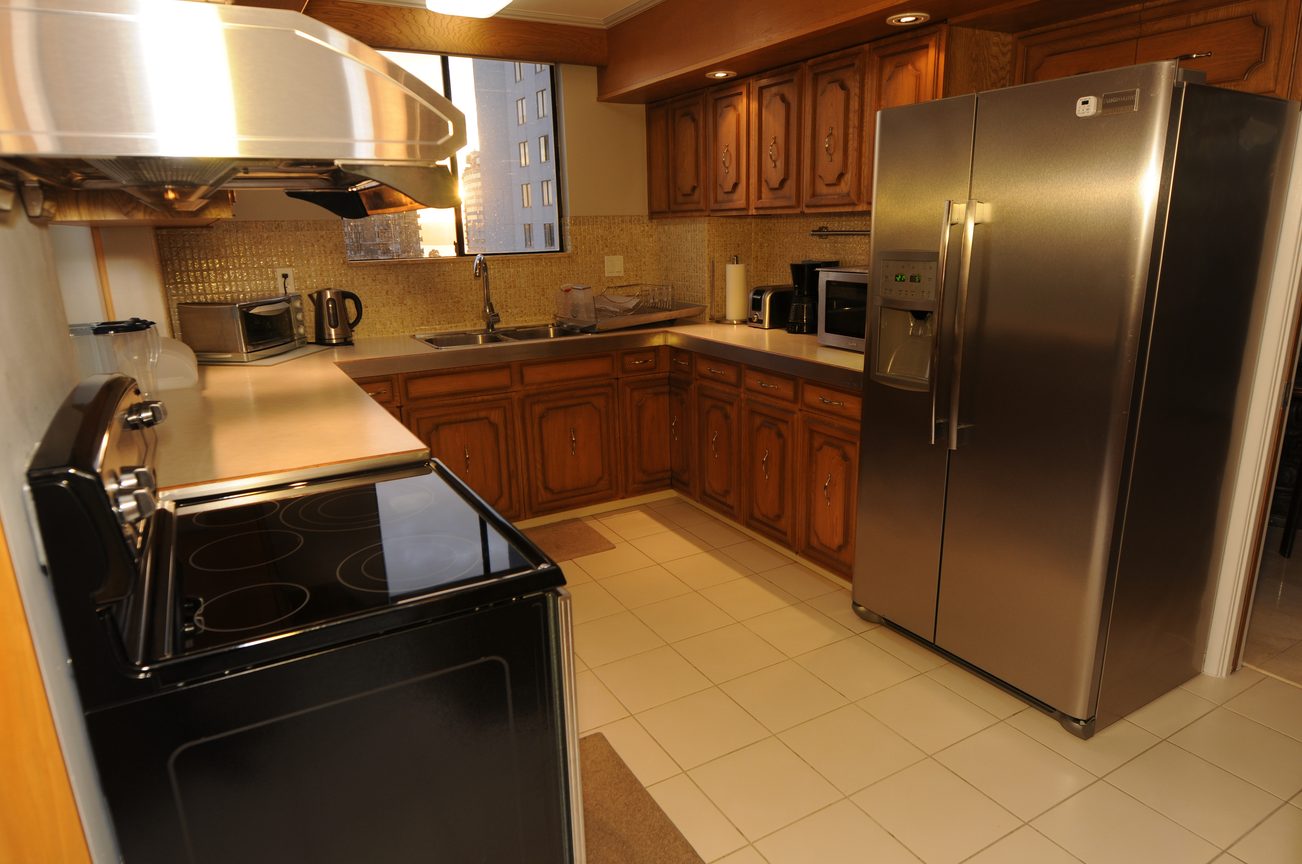 Bright kitchen with stainless steel appliances, wooden cabinets, and a city view through the window. - 1501 - 845 Chilco Street, Vancouver Downtown
