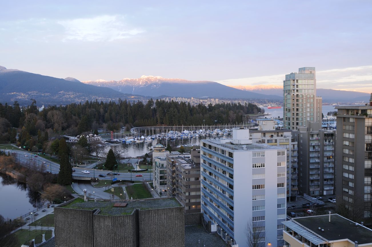 Bright living room with a stunning city view and marina, surrounded by modern buildings and snow-capped mountains.