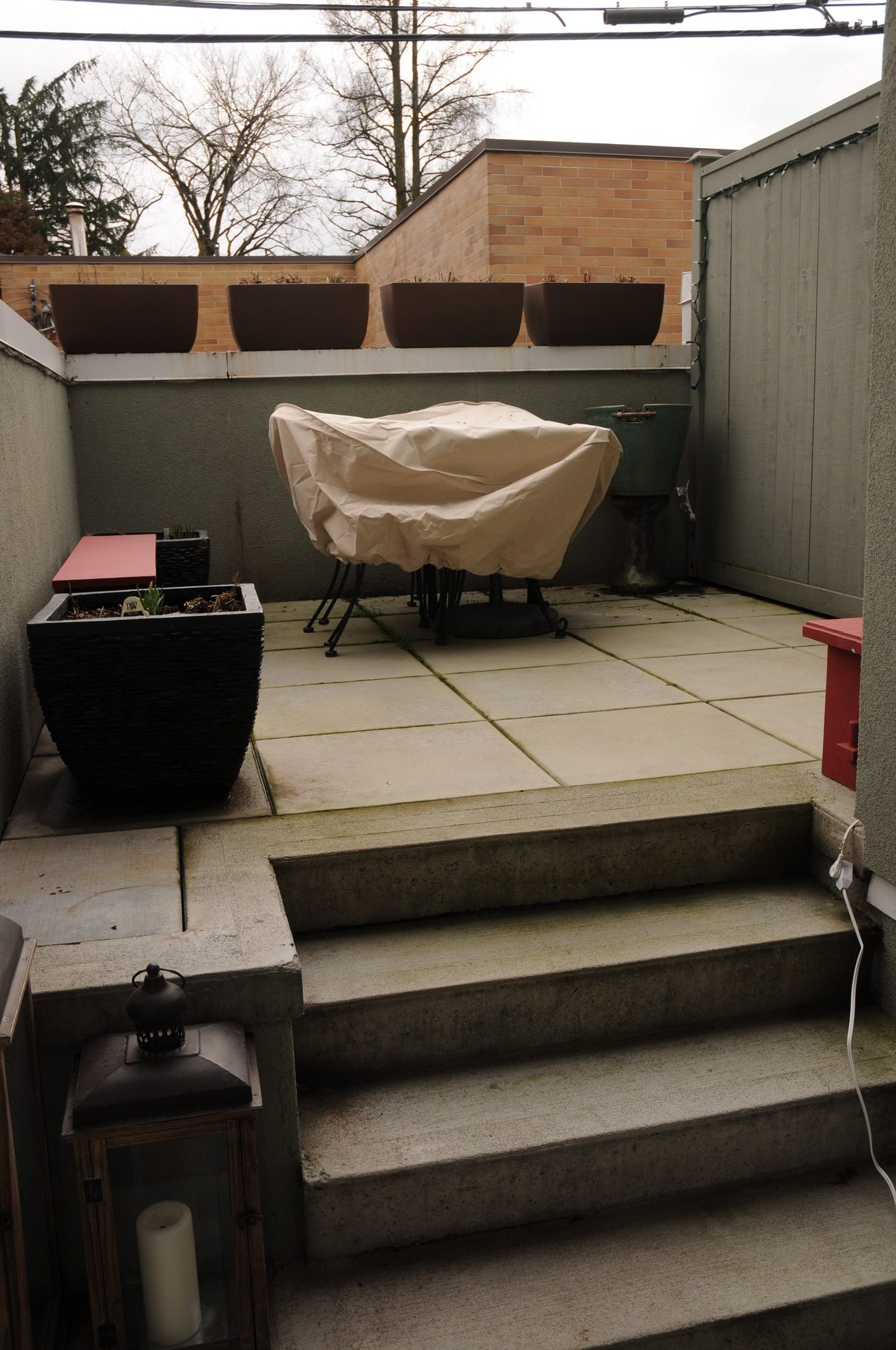 Furnished patio with covered table and potted plants, steps leading up. - 206 - 980 West 22nd Ave., Vancouver West Side