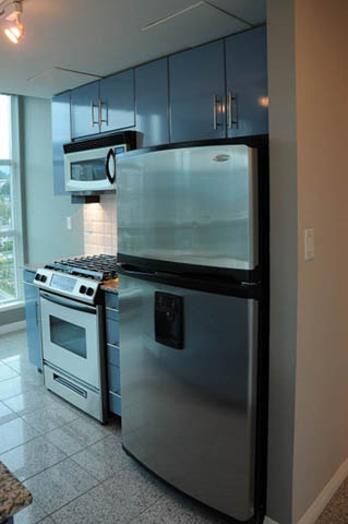 Bright kitchen with stainless steel appliances and blue cabinets, featuring a city view through the window.