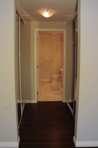 Bright hallway leading to a small bathroom with a toilet and shower, dark hardwood floors. - 1808 - 188 East Esplanade, North Vancouver