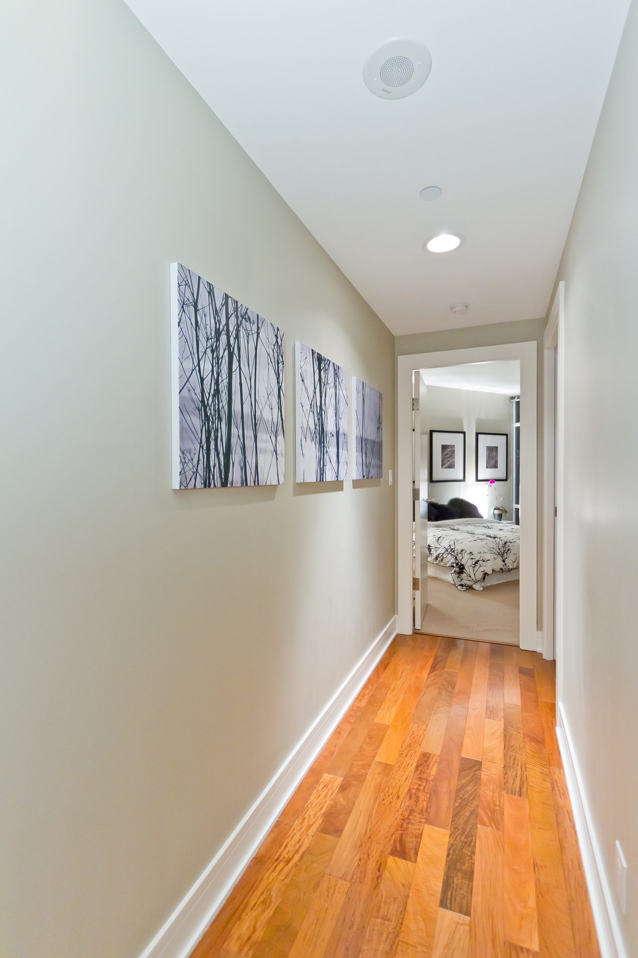 Bright hallway with hardwood floors leading to a cozy bedroom, featuring a black and white abstract artwork on the wall.