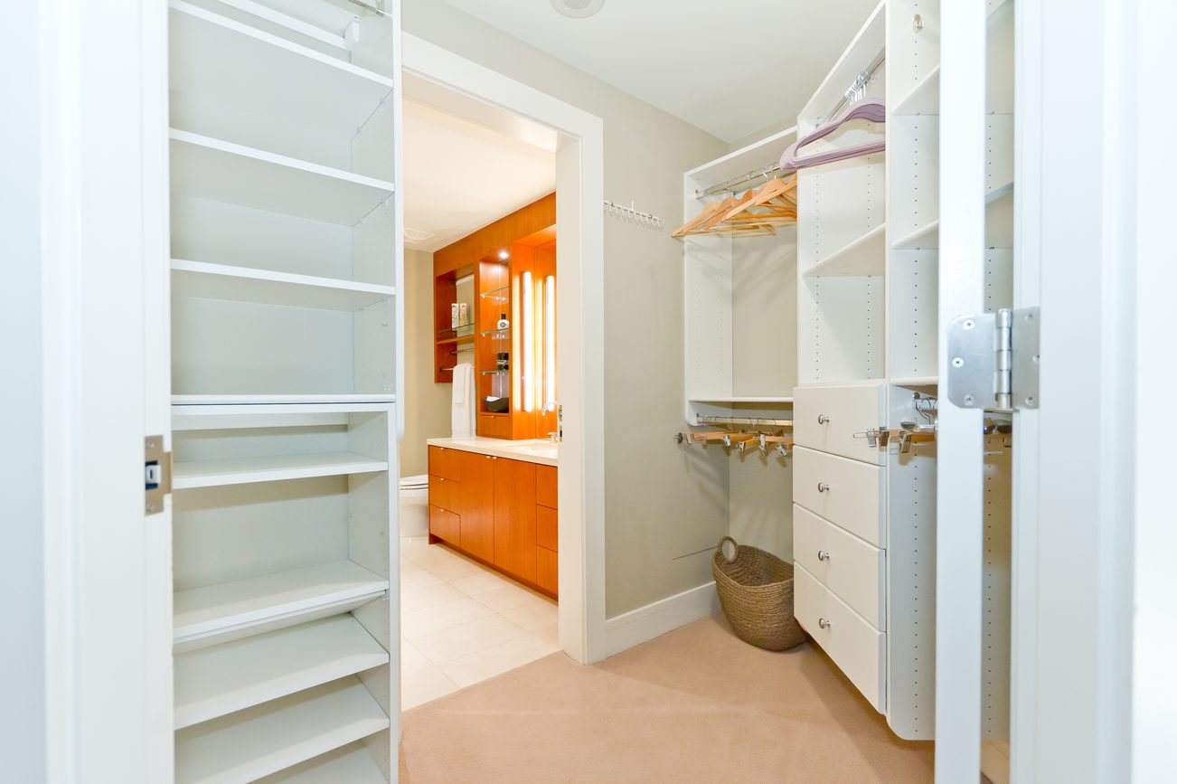 Bright walk-in closet with open shelves and hanging rods, leading to a bathroom with wooden cabinets. - 302 - 628 Kinghorne Mews, Vancouver Downtown