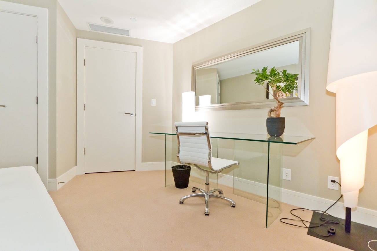 Bright and modern office with glass desk and white chair, featuring a large mirror and a potted plant. - 302 - 628 Kinghorne Mews, Vancouver Downtown