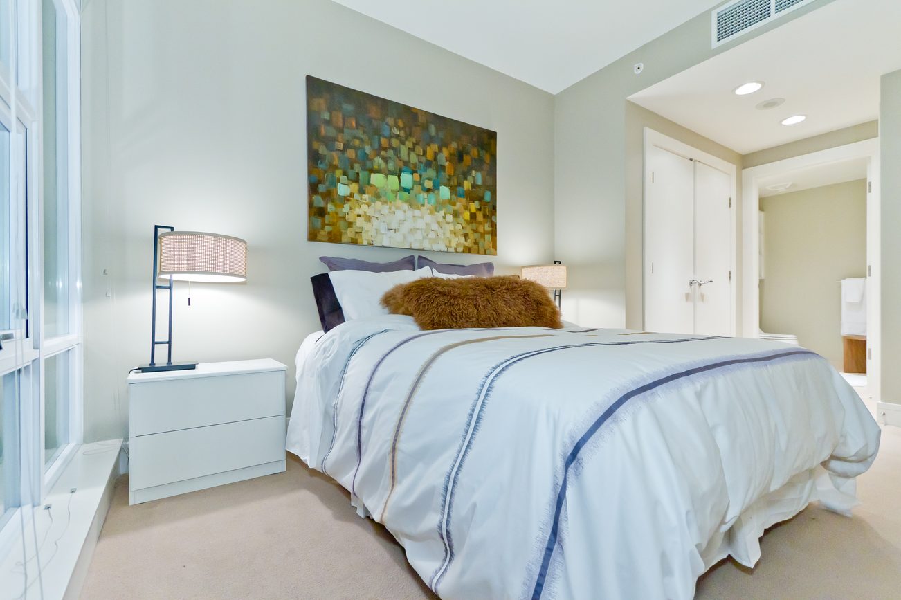 Spacious bedroom with modern decor, large artwork, and white bedding. - 302 - 628 Kinghorne Mews, Vancouver Downtown