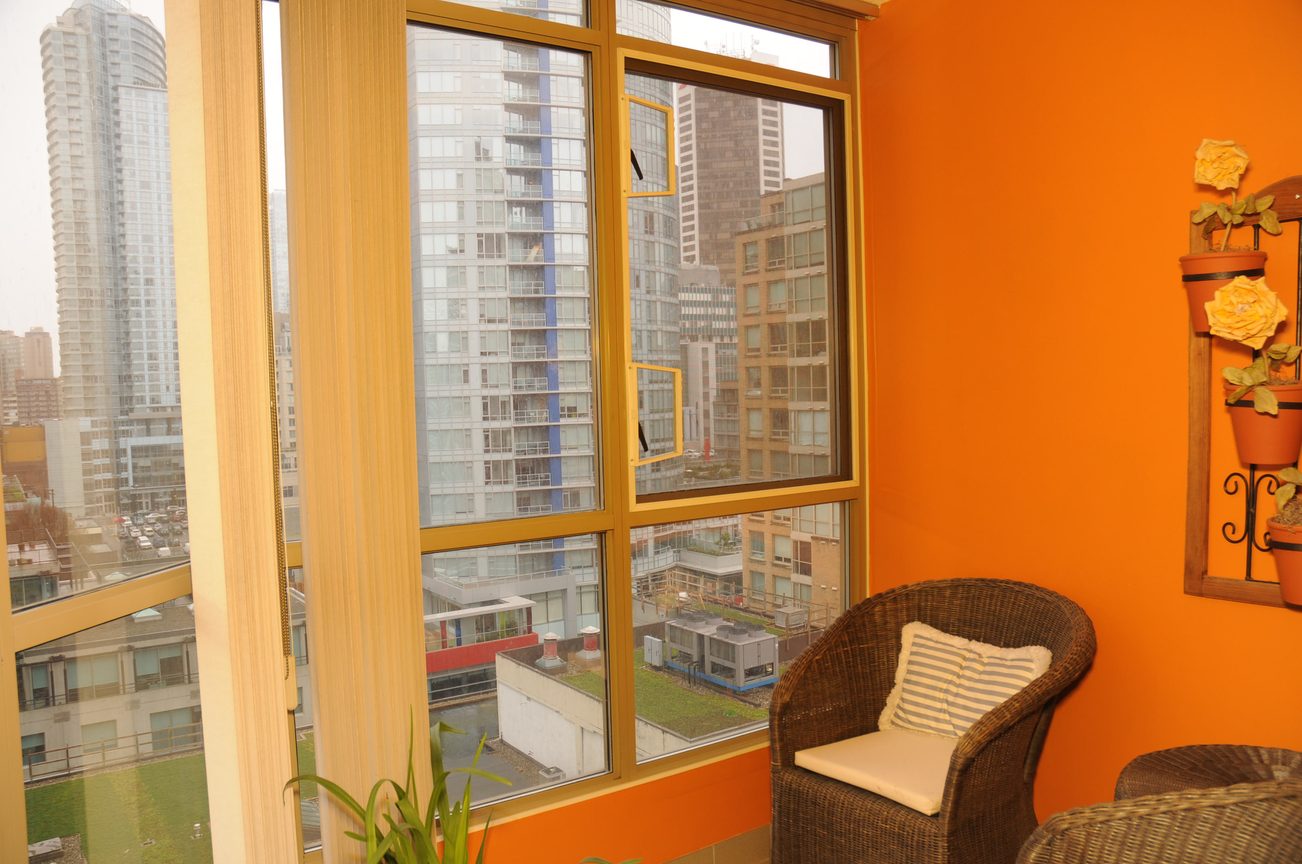Bright living room with city view and orange walls, furnished with wicker chairs. - 1705-867 Hamilton Street, Vancouver Downtown