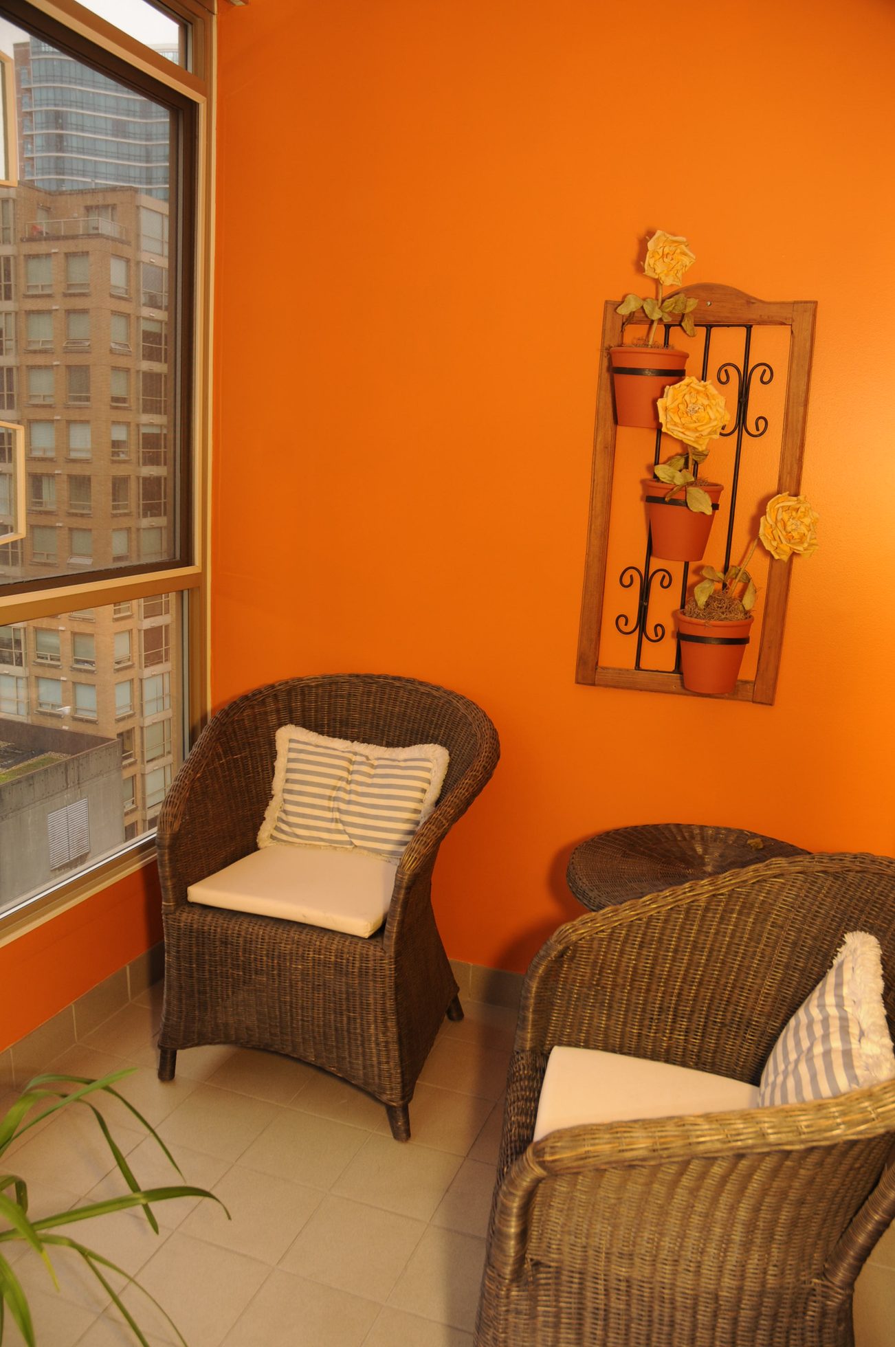 Furnished living area with orange walls, wicker chairs, city view, and decorative wall art. - 1705-867 Hamilton Street, Vancouver Downtown