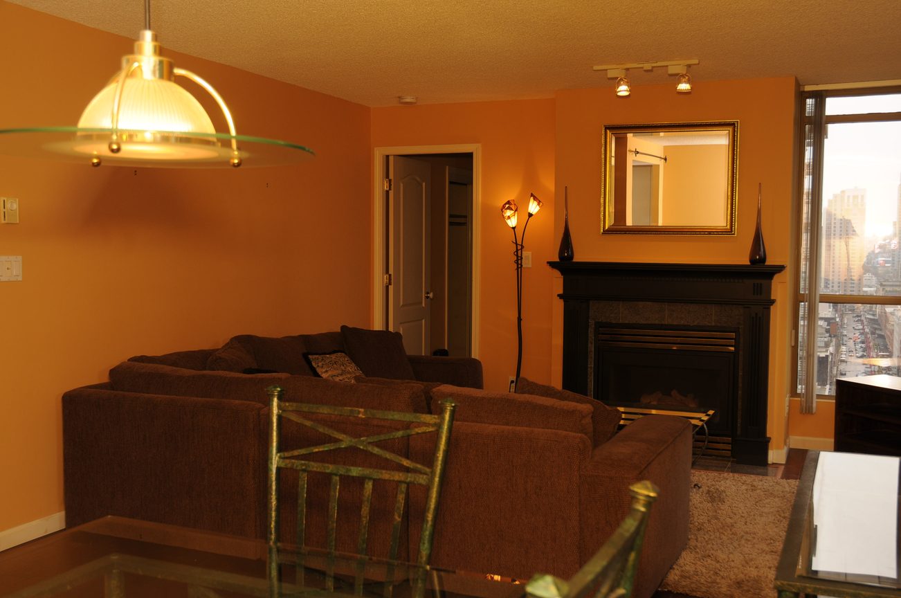 Furnished living room with city view, orange walls, and a black fireplace. - 1705-867 Hamilton Street, Vancouver Downtown