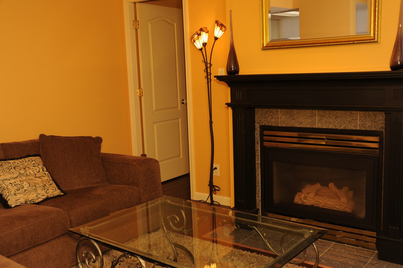Furnished living room with a glass coffee table, brown sofa, and a lit fireplace. - 1705-867 Hamilton Street, Vancouver Downtown