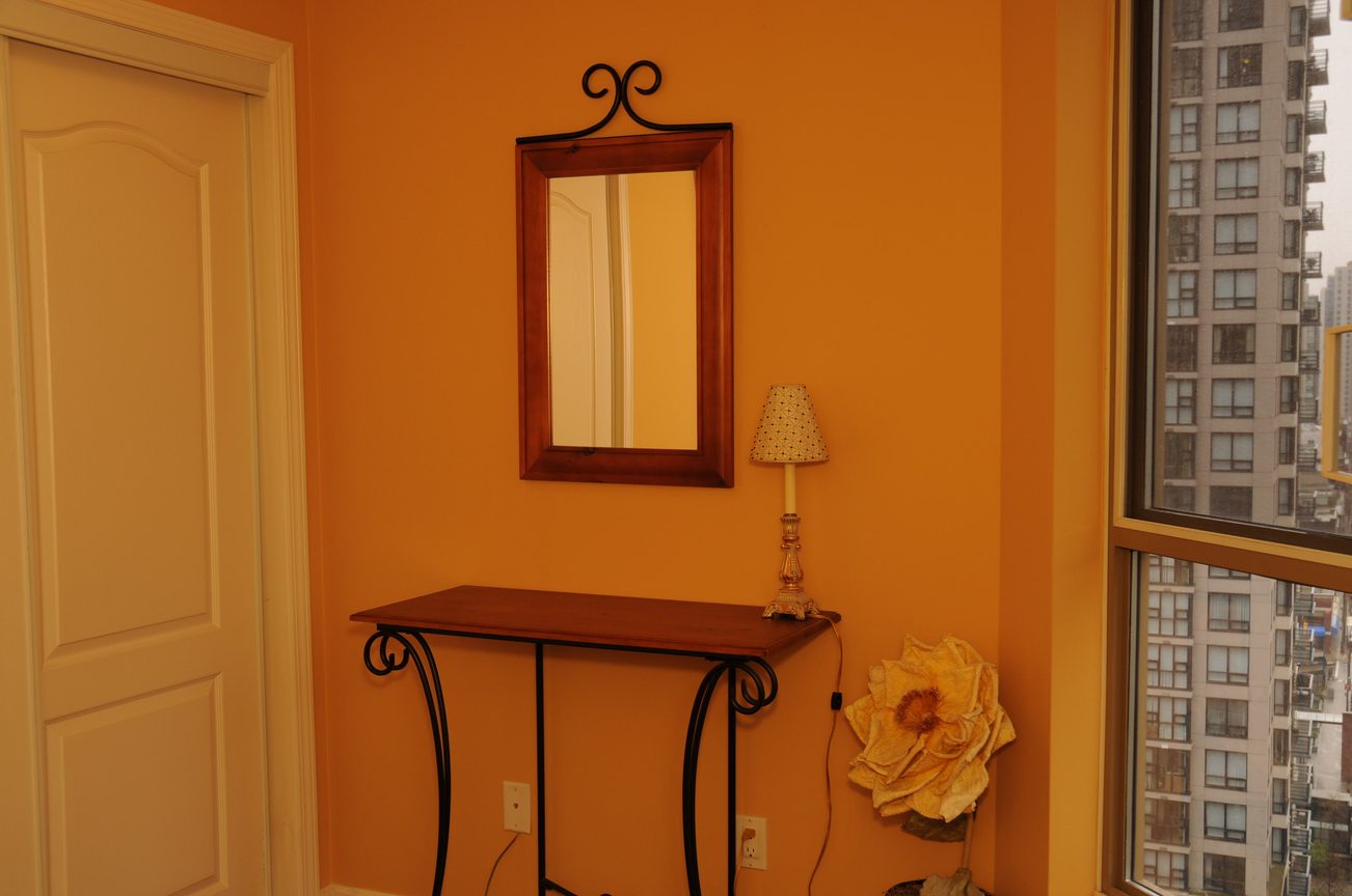 Bright bedroom with orange walls, city view, and a wooden nightstand. - 1705-867 Hamilton Street, Vancouver Downtown