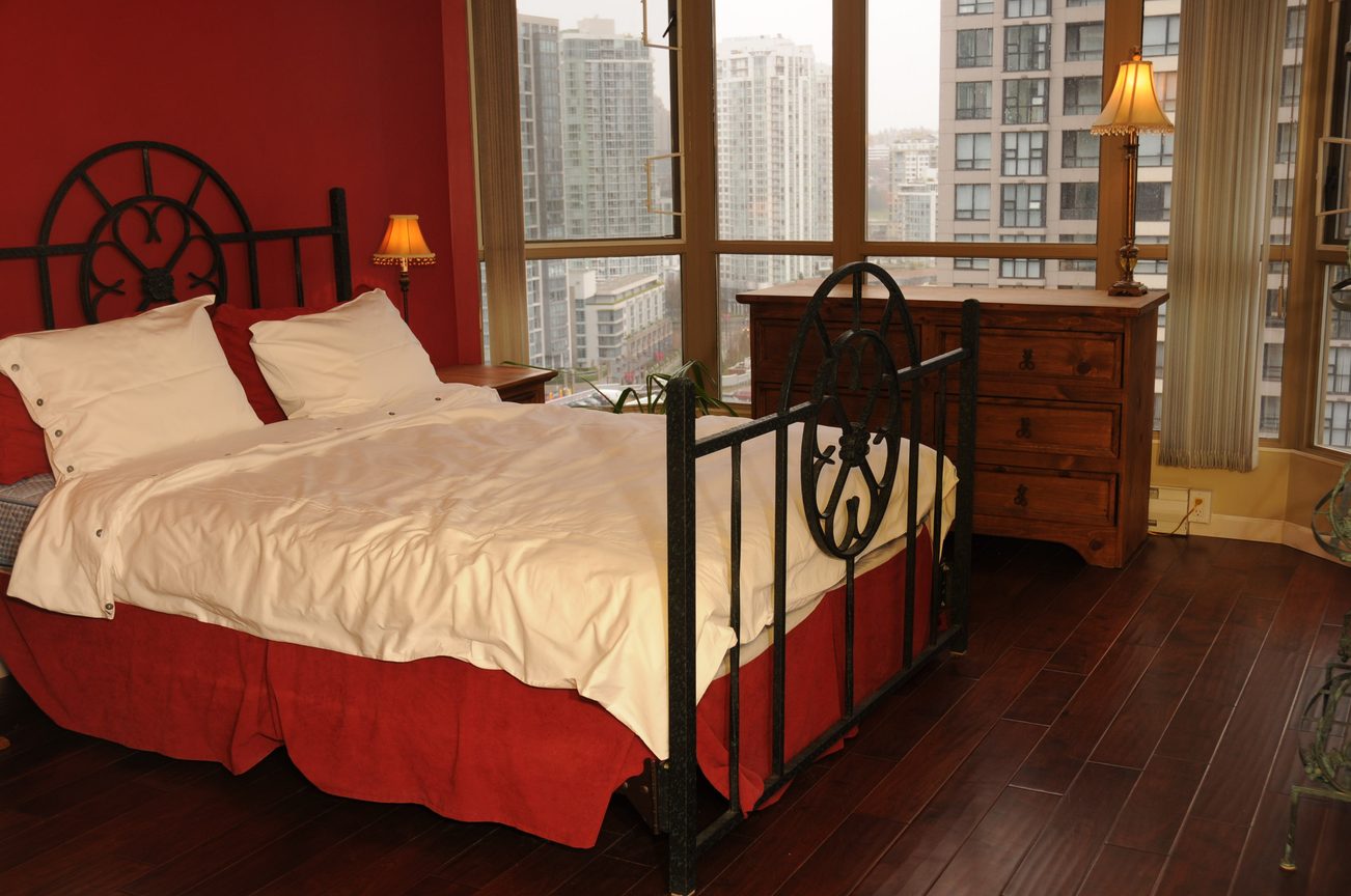 Bright bedroom with city view, hardwood floors, and a double bed with red accents. - 1705-867 Hamilton Street, Vancouver Downtown
