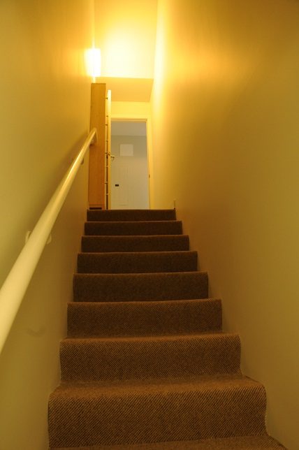 Carpeted staircase leading to a door, warm lighting. - 1275 Alberni Street, Vancouver Downtown