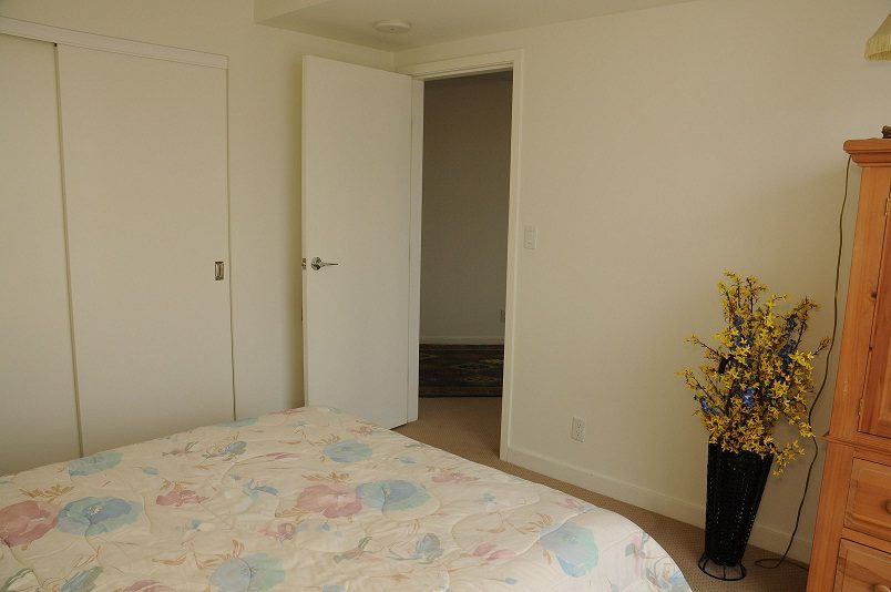 Bright bedroom with floral bedding and a vase of yellow flowers, leading to a den area. - 2006 - 918 Cooperage Way, Vancouver Downtown